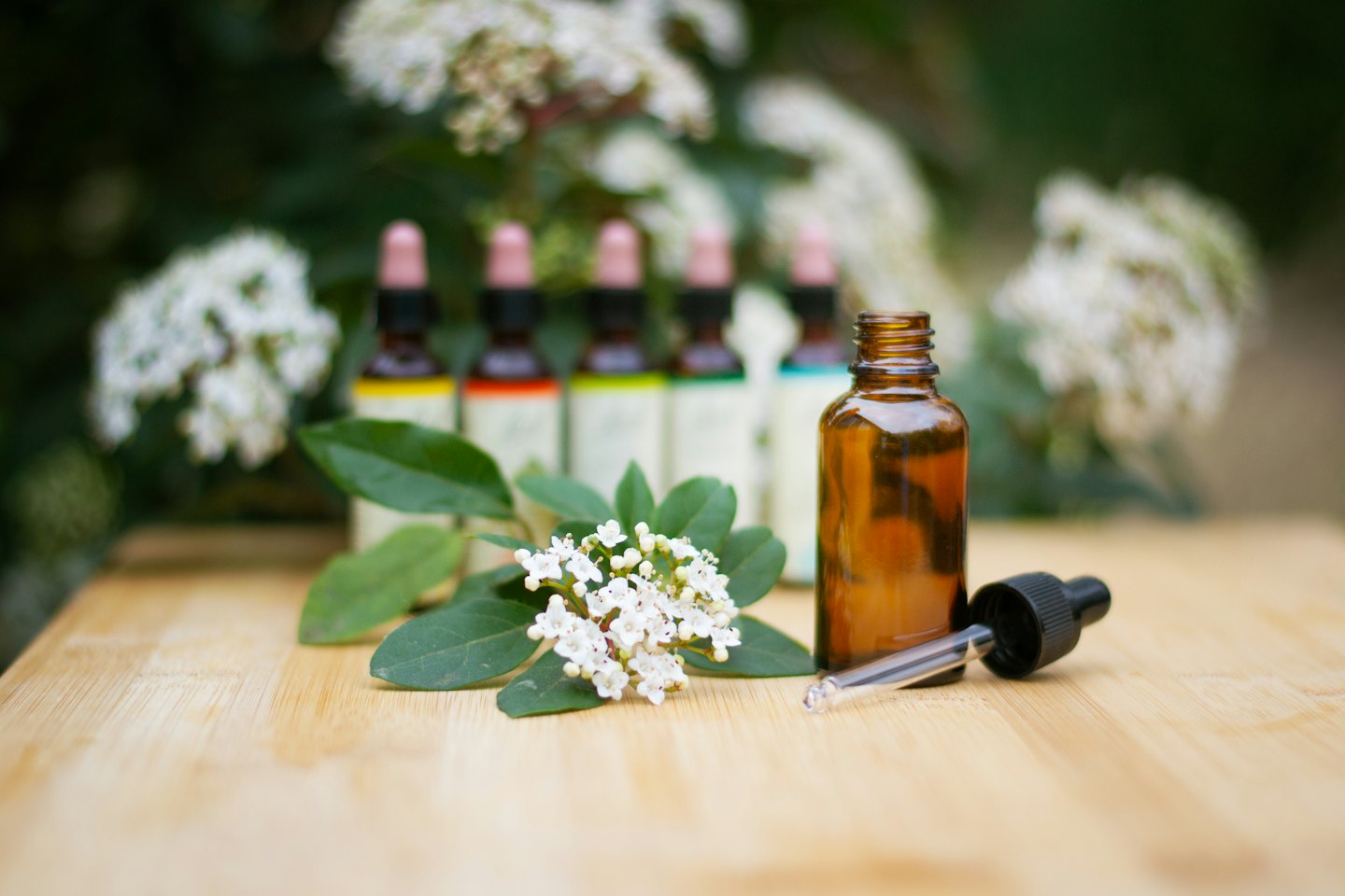 Amber glass dropper bottles sit on a wooden surface with flowers.